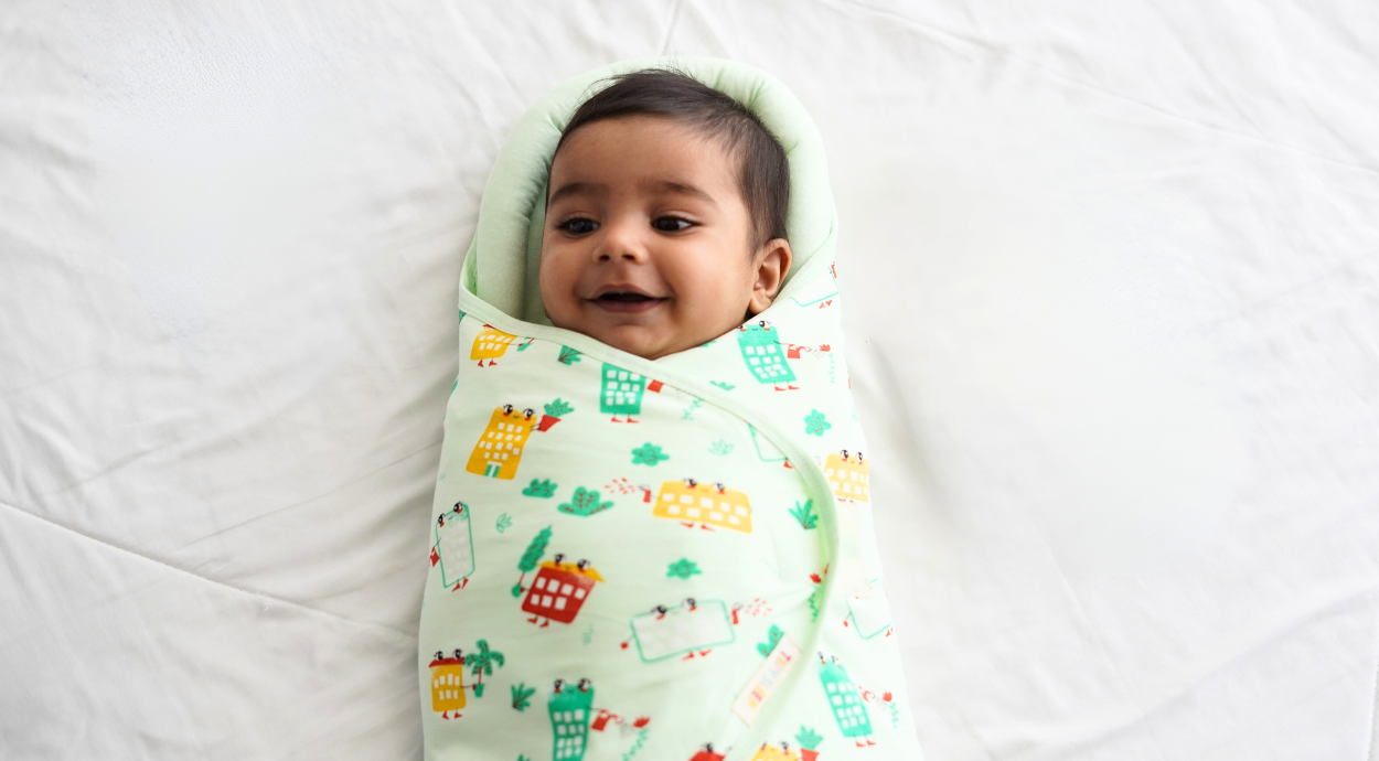 A baby wrapped in a pod wrapper lying in a white bedsheet