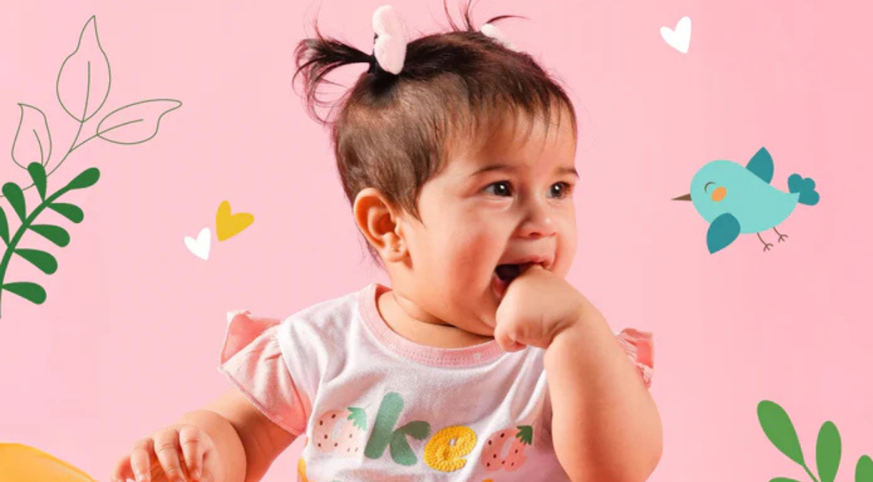 A toddler in a pink shirt with strawberry designs sits against a bright pink background, surrounded by playful illustrations of leaves and a bird.