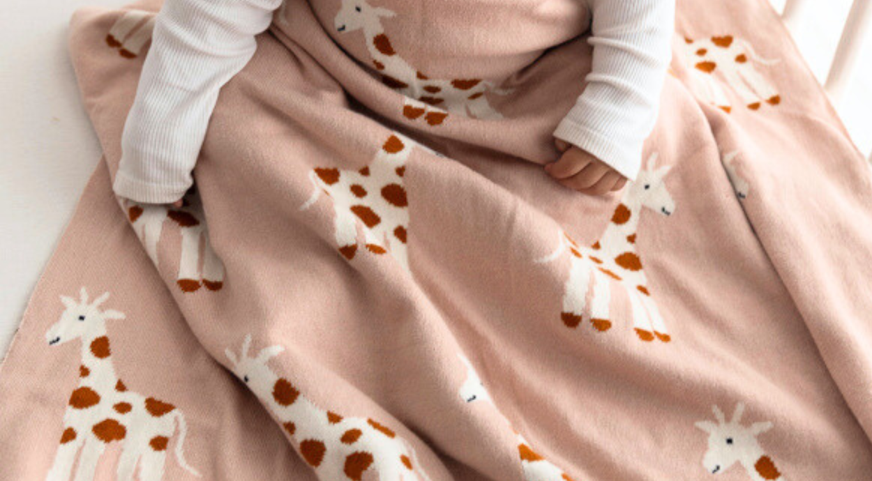 A child wrapped in a peach blanket adorned with cute giraffe patterns, sitting comfortably on a soft surface.