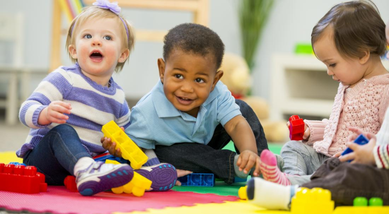 Four young children are playing on a colorful mat with building blocks, engaged in a creative activity together.