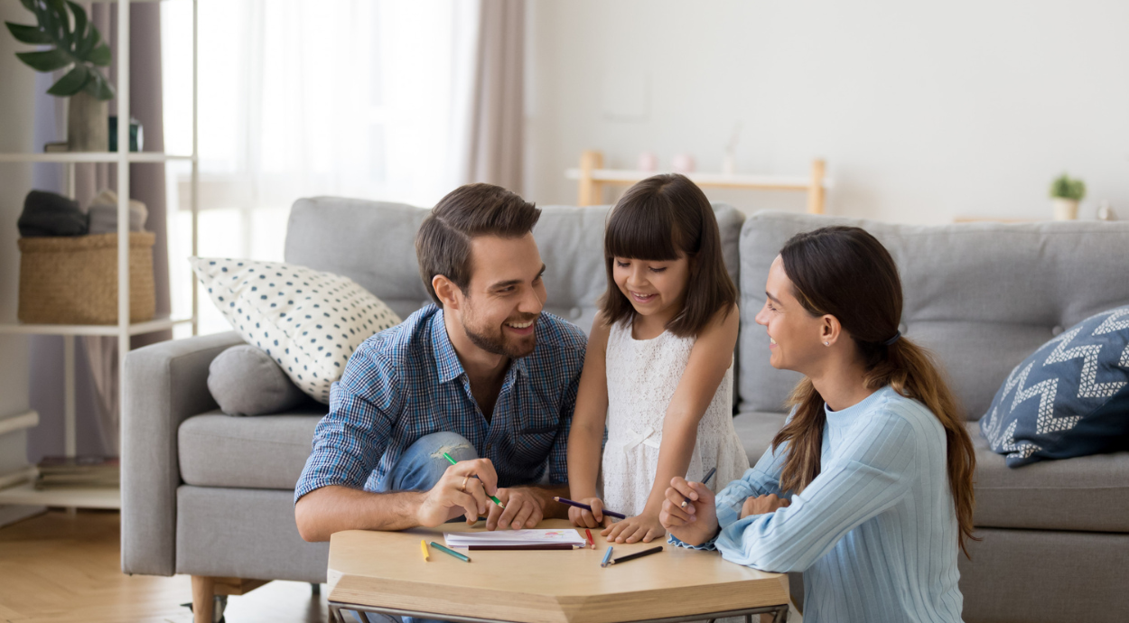 A family sits together around a coffee table, engaged in drawing and coloring, surrounded by a cozy living room.