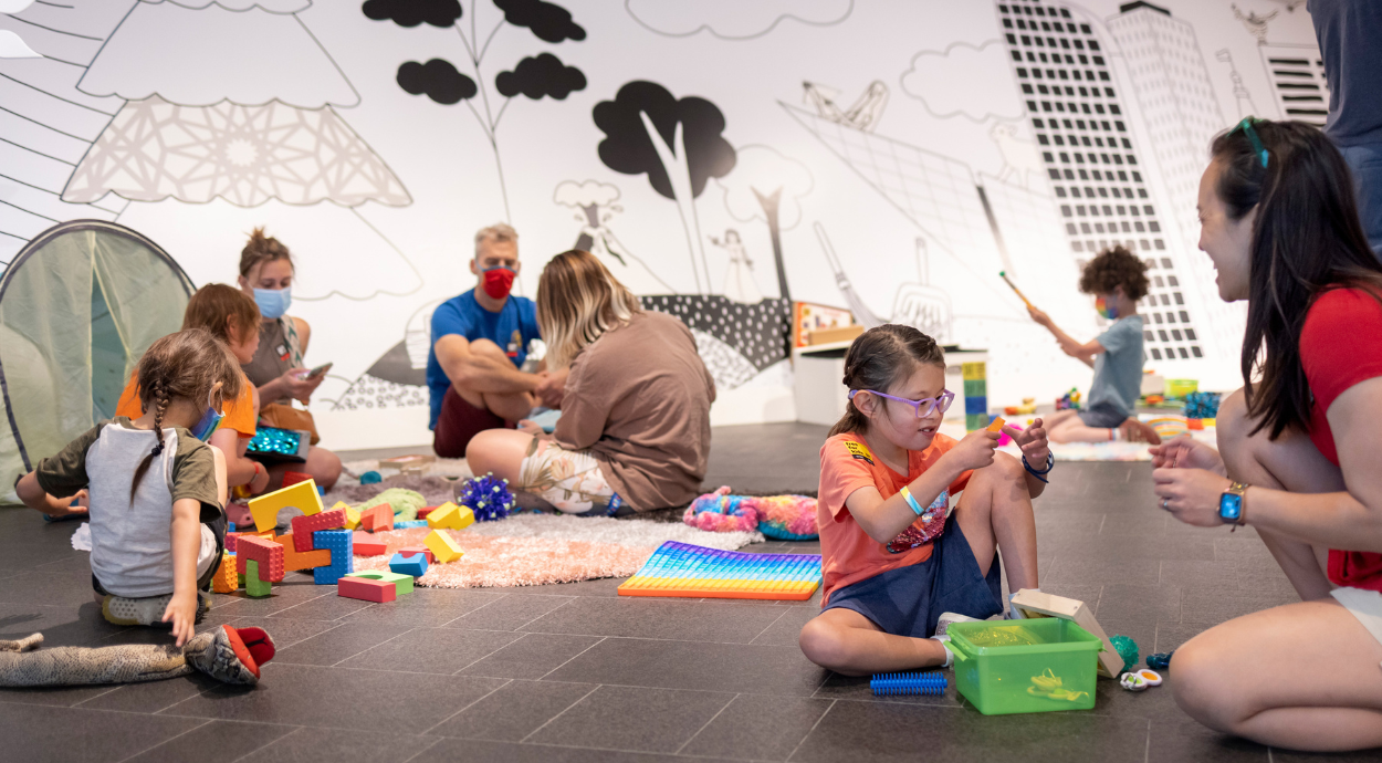 Children play and create with colorful building blocks and toys on the floor of a vibrant, artistic playroom.