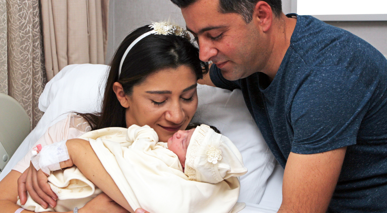 Parents lovingly embracing their newborn baby in a hospital room, sharing a tender moment.
