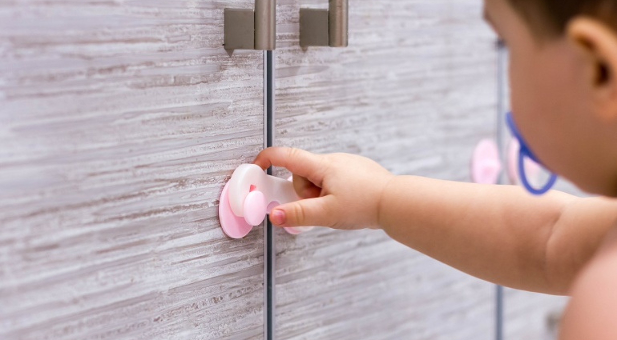 A small child’s hand reaches for a pink suction cup latch on a tiled cabinet, emphasizing a safe and playful environment.