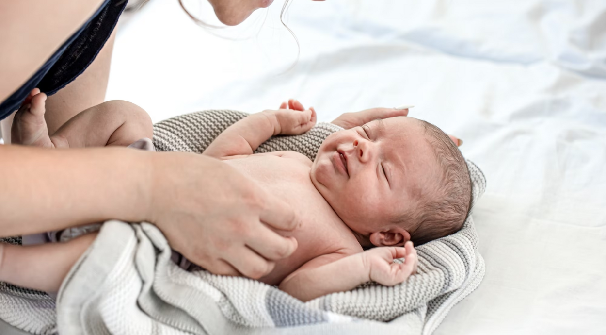 A caring parent interacts with a wrapped newborn on a soft blanket, showcasing tenderness and connection.