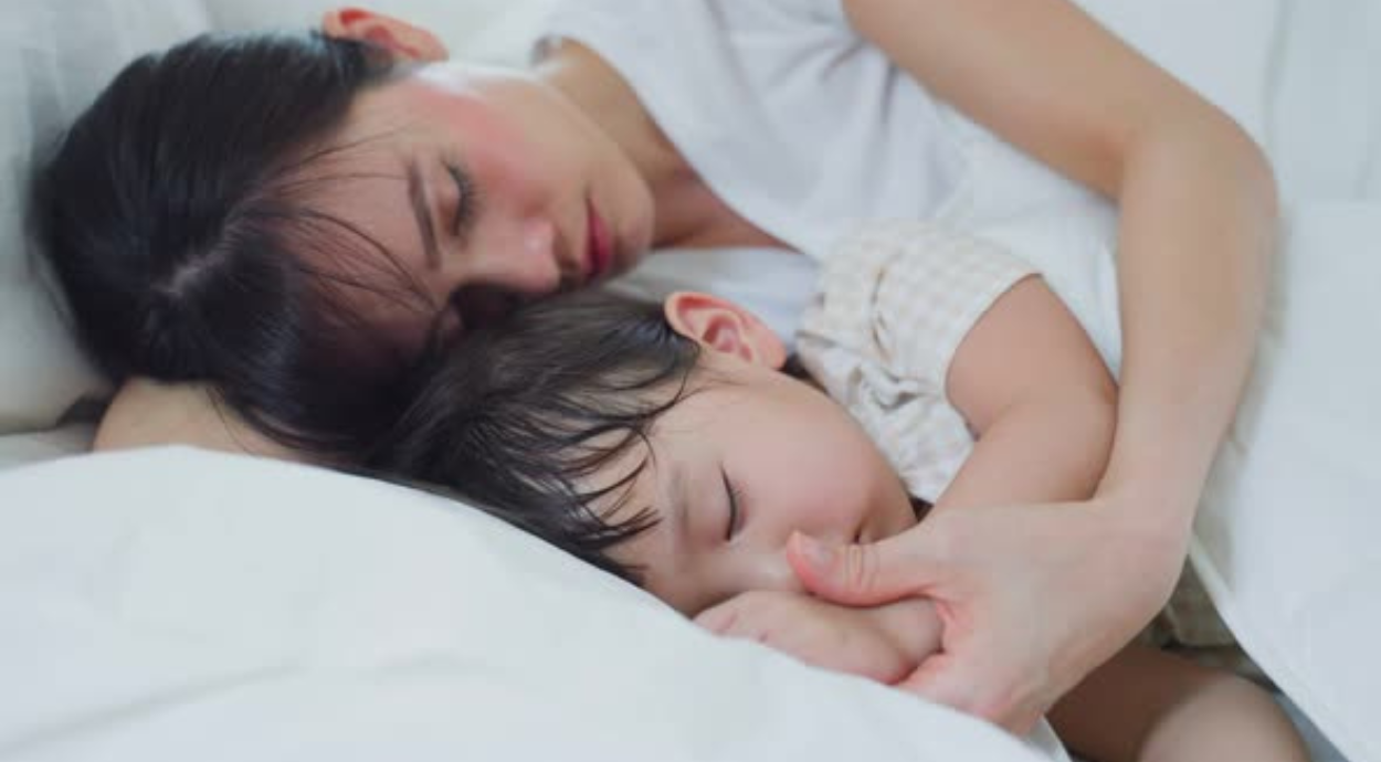 A mother gently sleeps with her young child, embracing each other under soft blankets in a serene moment of love and comfort.