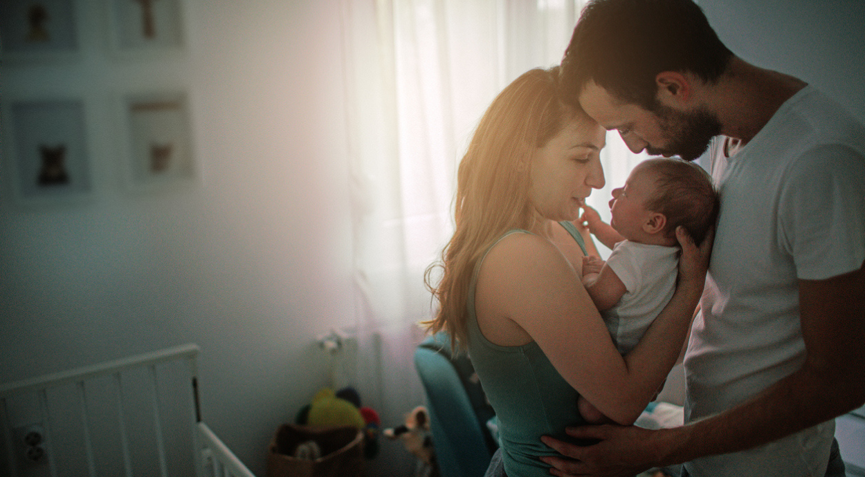 A couple lovingly holds their baby in a softly lit nursery, showcasing warmth and tenderness in a serene atmosphere.