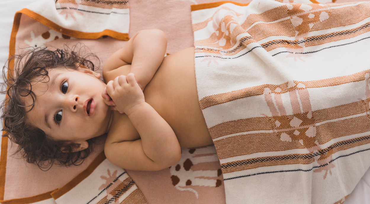 a baby boy covered in a colorful knitted blanket