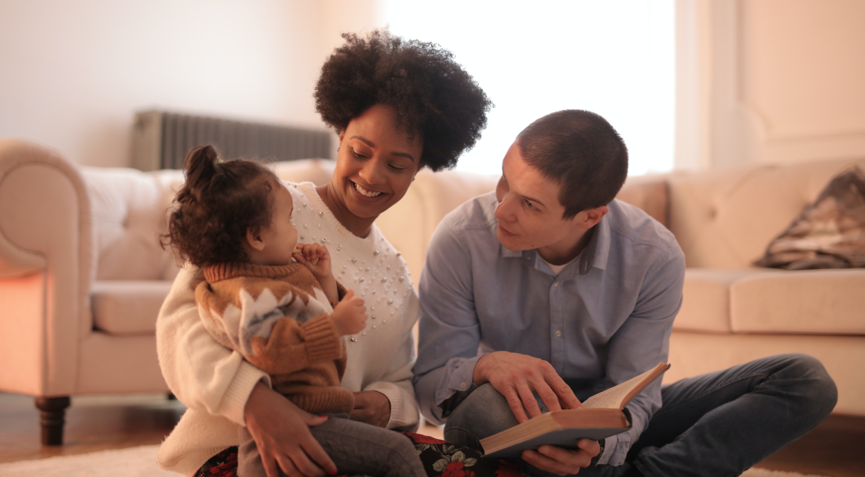 A family sits together on a cozy rug, reading a book, with a warm and inviting living room in the background.