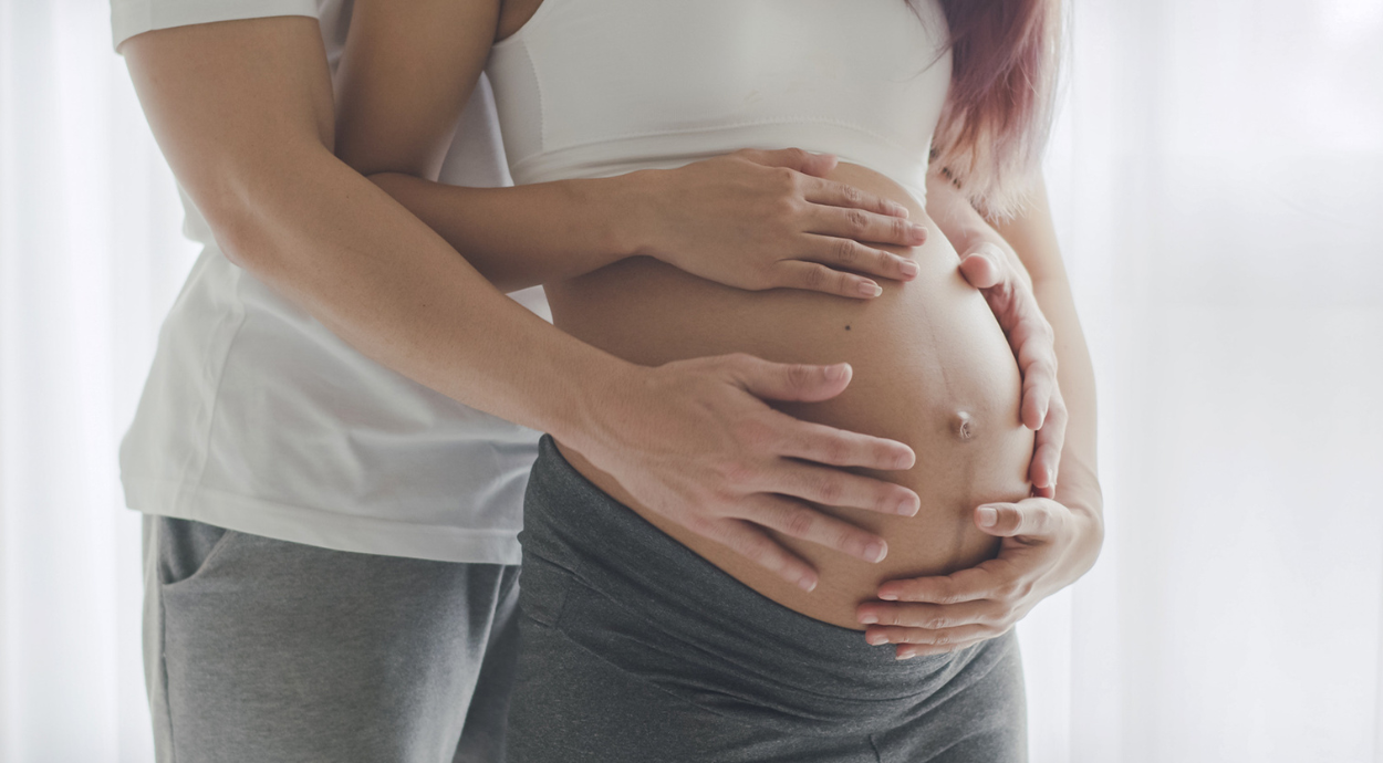 A couple embraces, gently resting their hands on the woman's pregnant belly, symbolizing love and anticipation of new life.