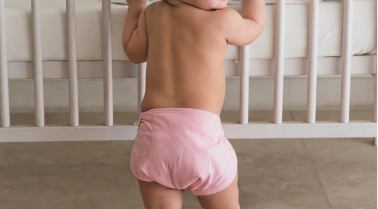 A baby standing in a pink cotton nappy