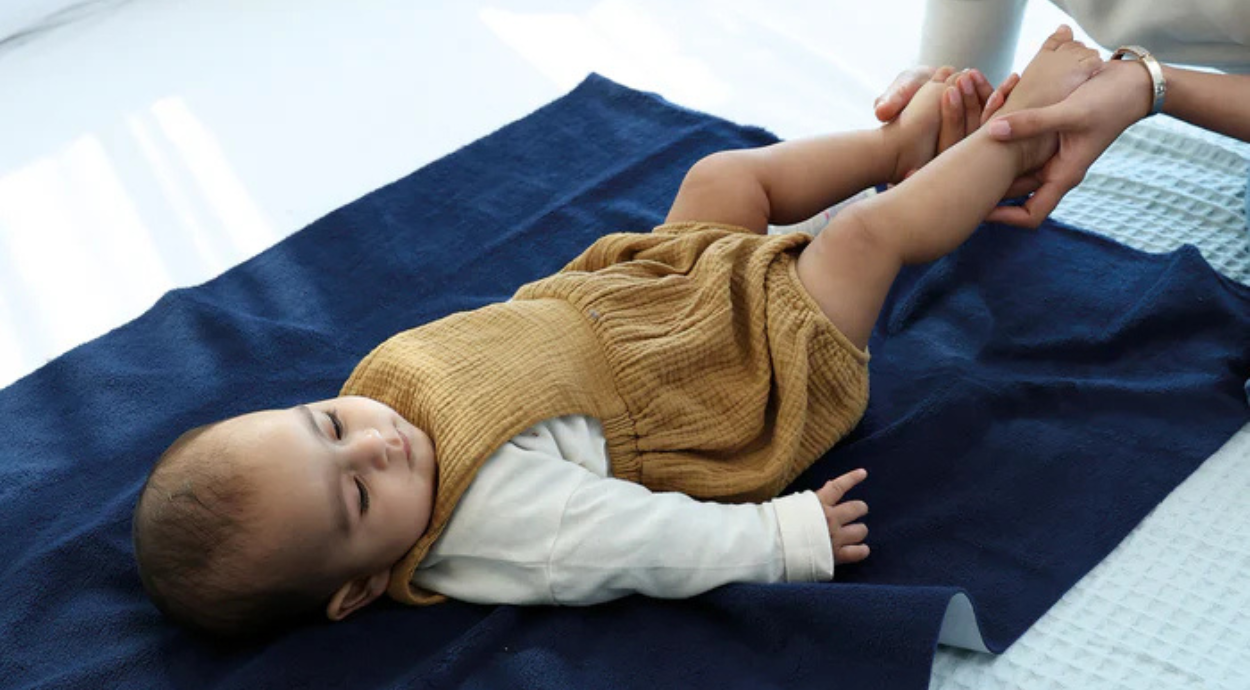 A baby girl lying on a navy blue dry sheet and a woman holding her legs