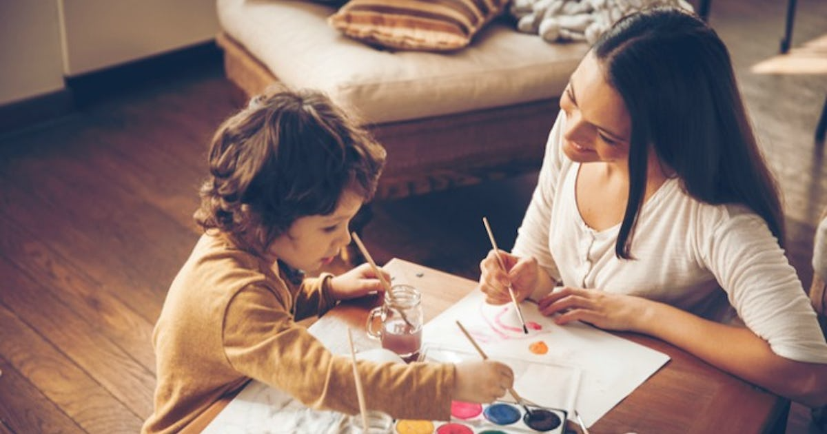 A child and an adult engaged in a creative painting activity at a wooden table, surrounded by art supplies and a cozy room atmosphere.