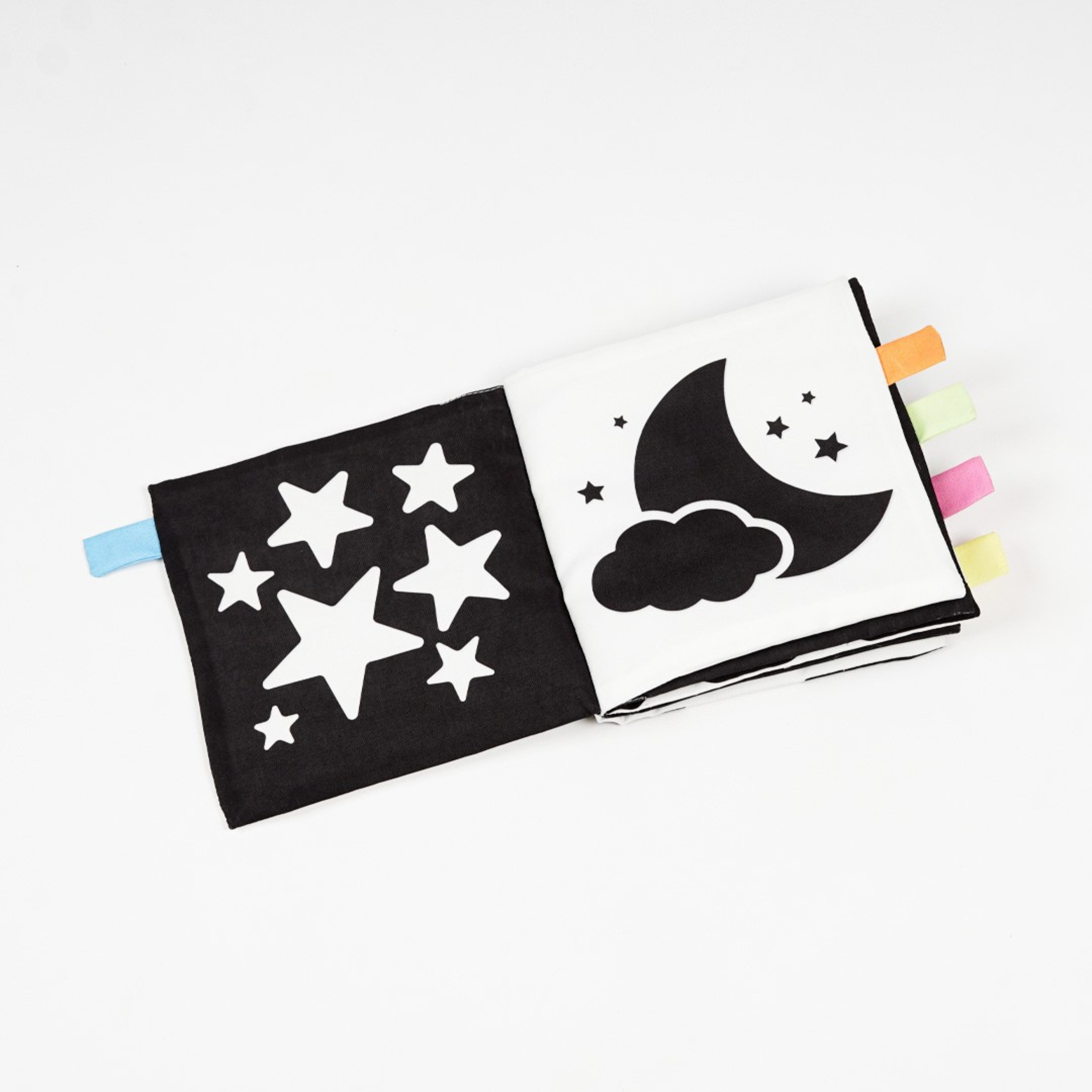 A fabric baby book featuring black and white pages with star and moon designs, including colored tabs on the side for easy handling.