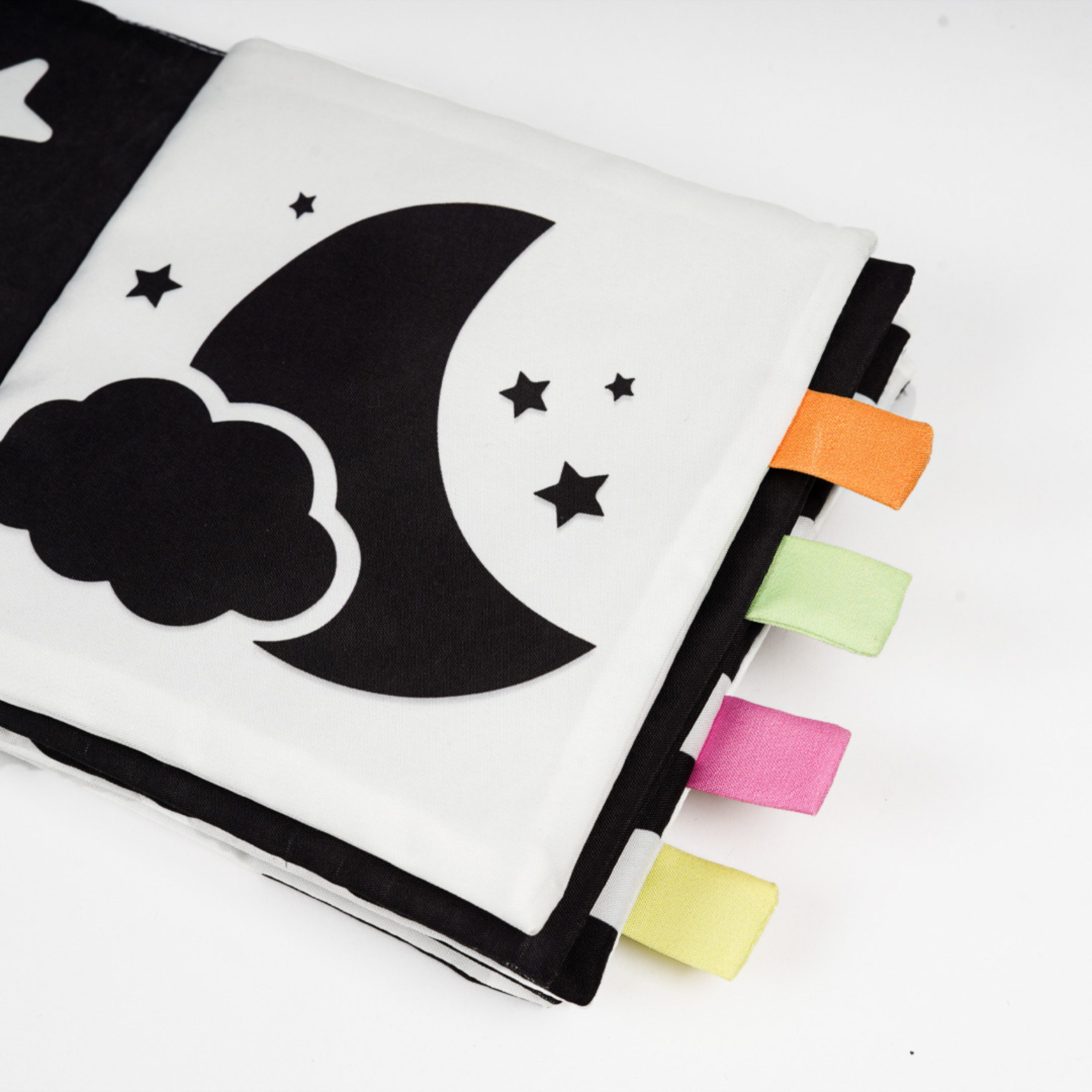 A close-up of a black and white children's fabric book featuring a crescent moon, stars, and colorful tag ribbons.