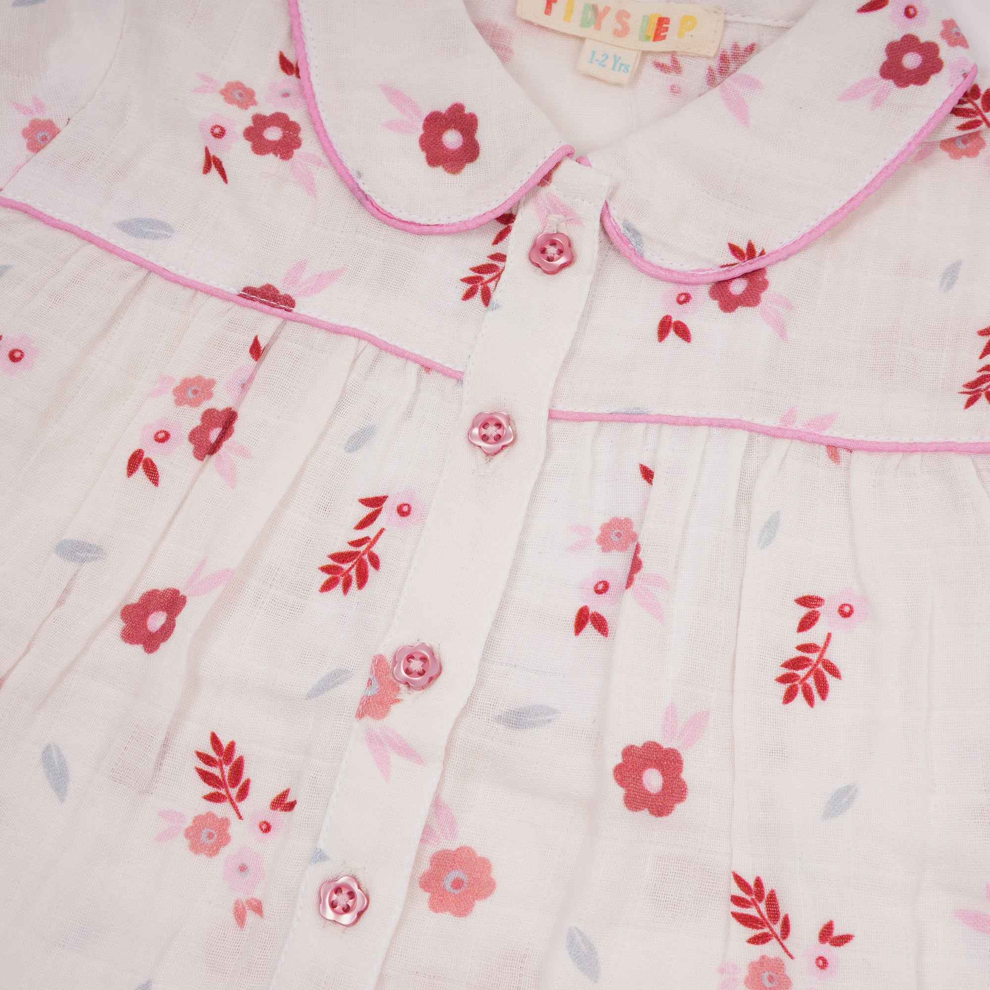 Closeup of a baby's cotton muslin nightsuit with a long-sleeve top featuring a red and pink floral pattern.