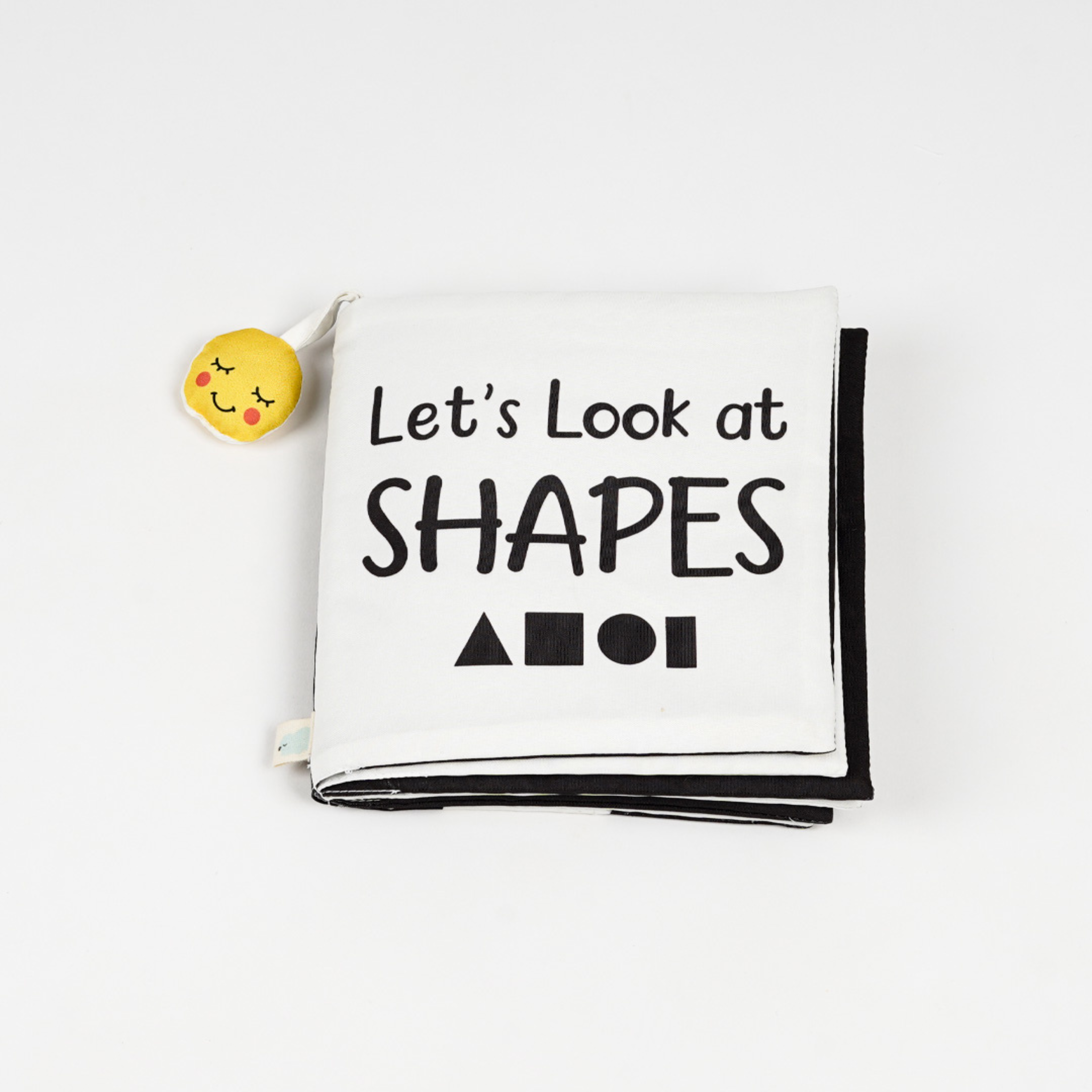 A colorful baby cloth book titled "Let's Look at SHAPES," featuring playful text and a smiling yellow plush toy on the corner.