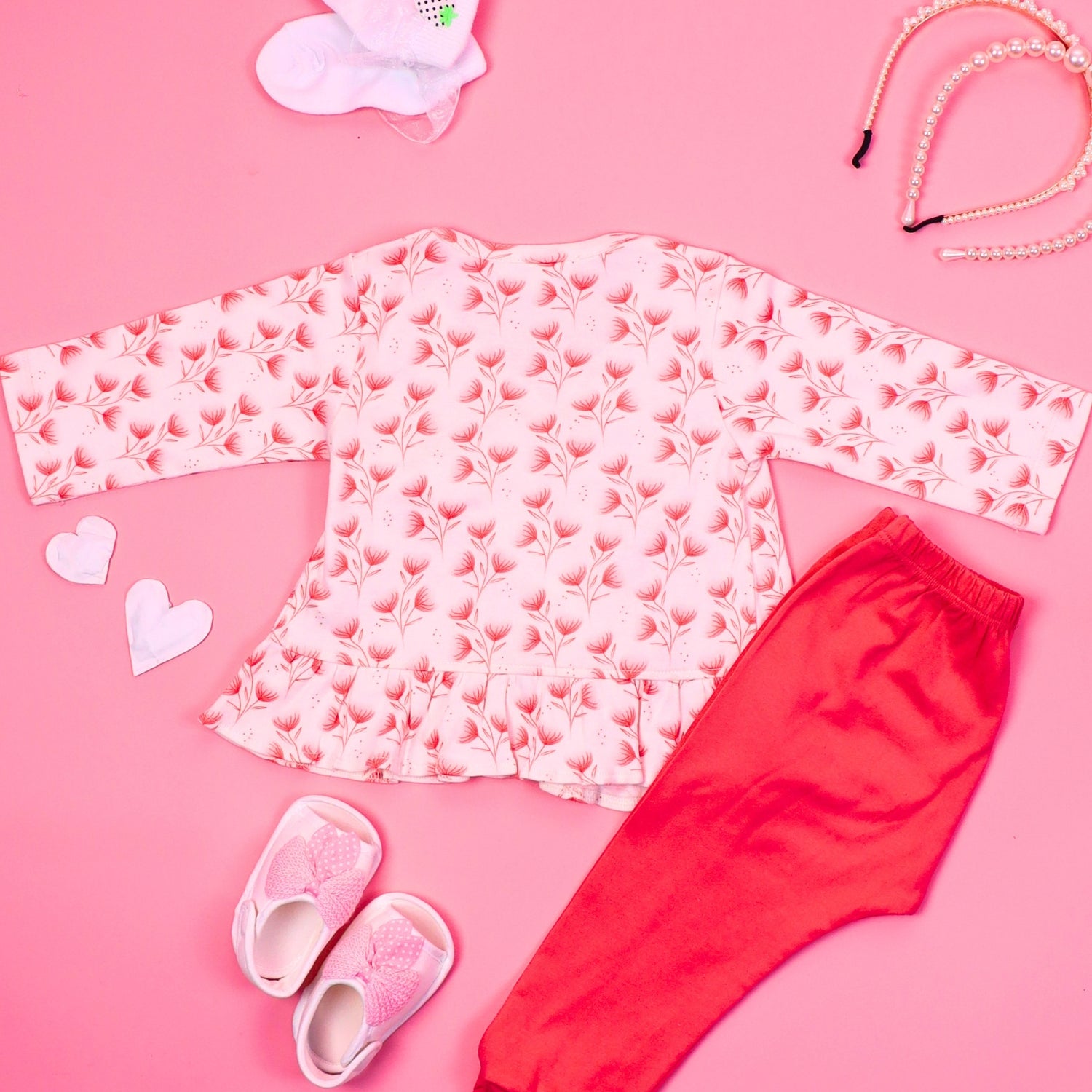 Back view of pink floral night suit set with a wrap-style top and matching red pants, displayed on a pink background with accessories like pearl necklaces, baby shoes, and a hairband.