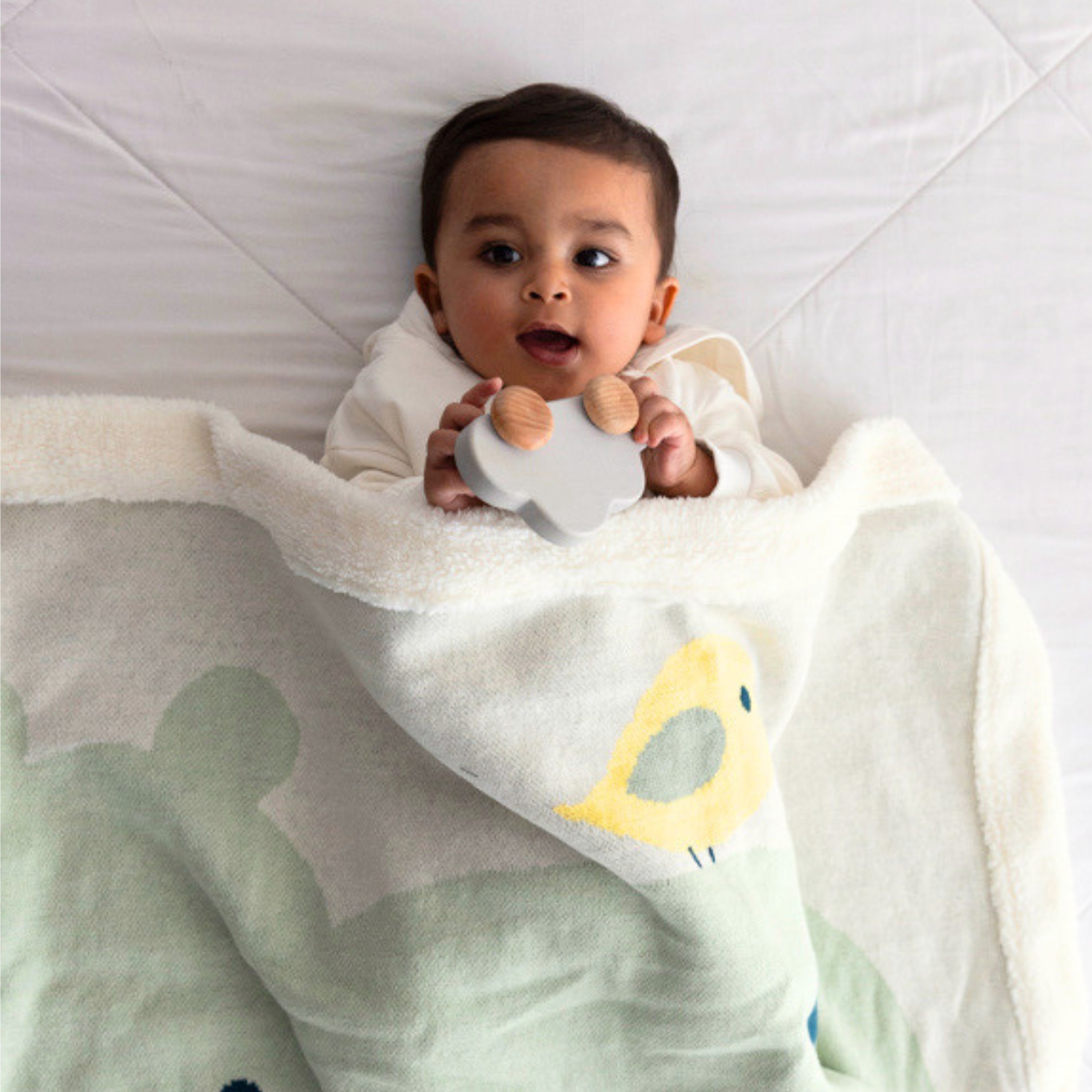 Baby lying in bed & wrapped in a soft green & white fleece blanket, showcasing cozy warmth and comfort.