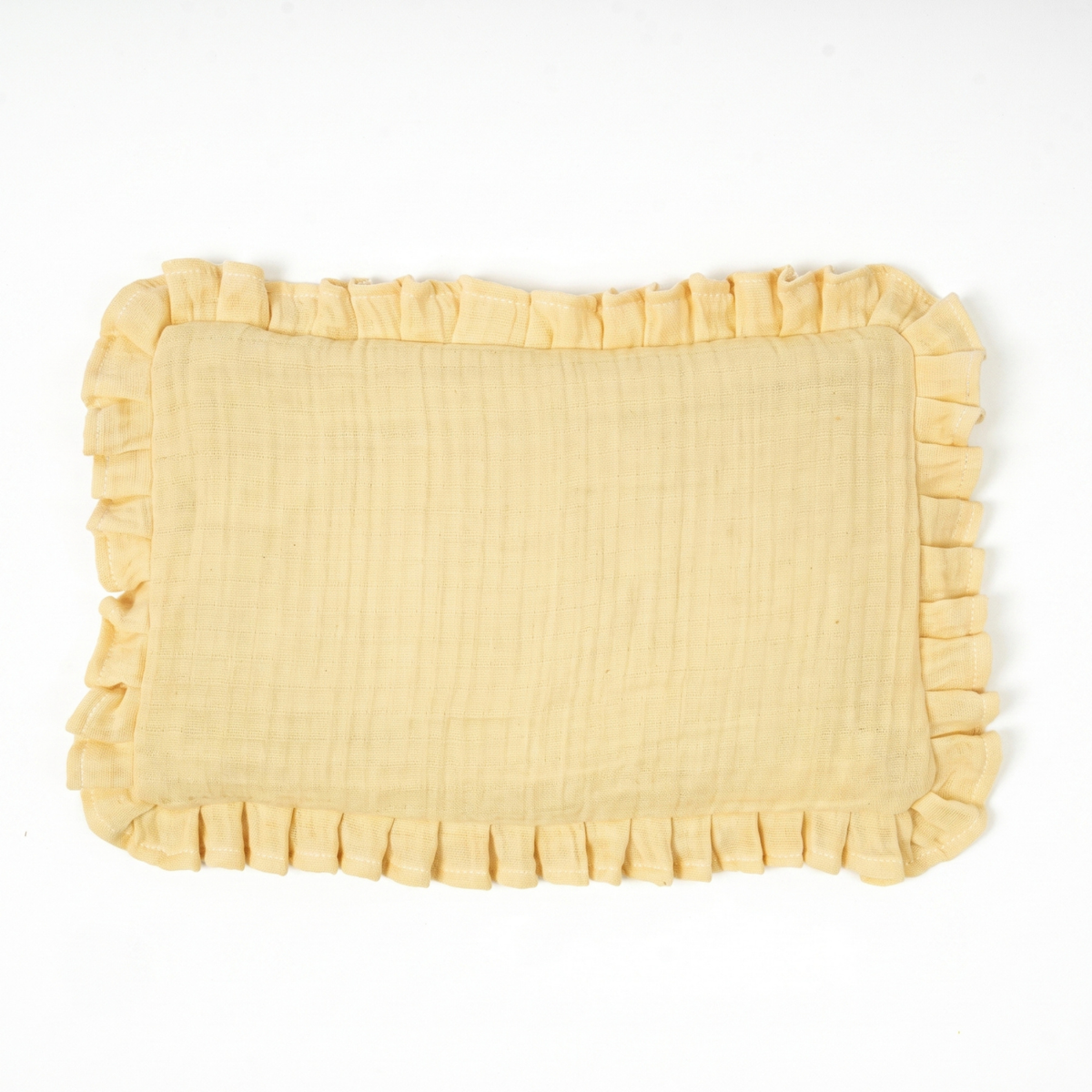 A butter yellow mustard seed baby pillow with a ruffled border, laid flat on a white background.