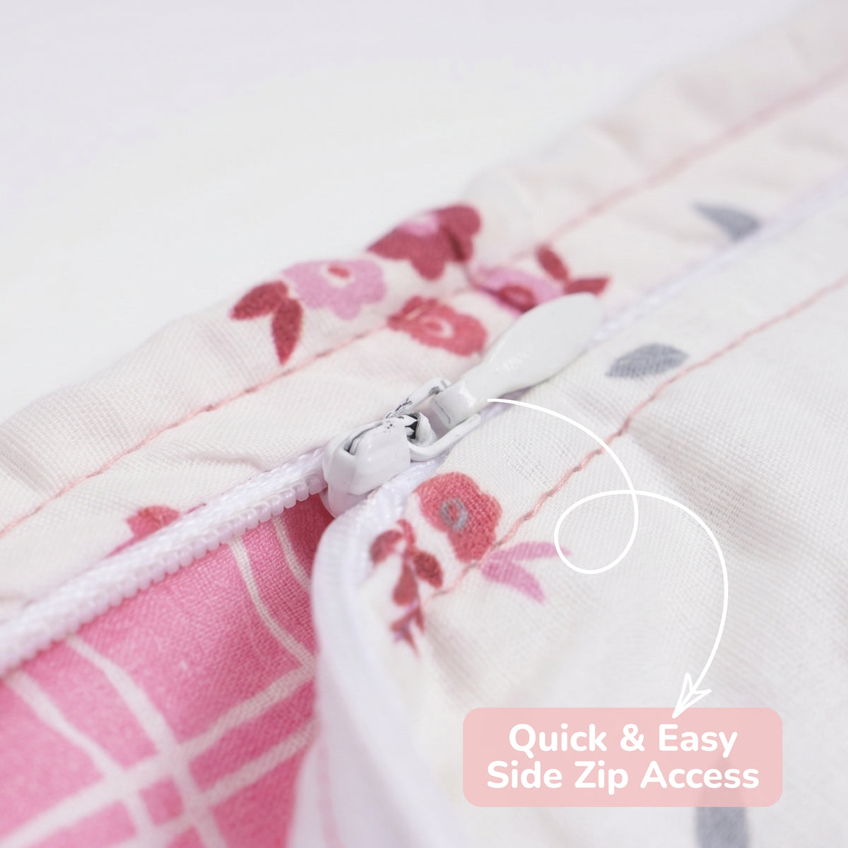 Close-up of a baby sleep sack with a floral print in pink, red, and gray on a white background, showing a side zipper with a white pull tab and an overlay text reading 'Quick & Easy Side Zip Access'.
