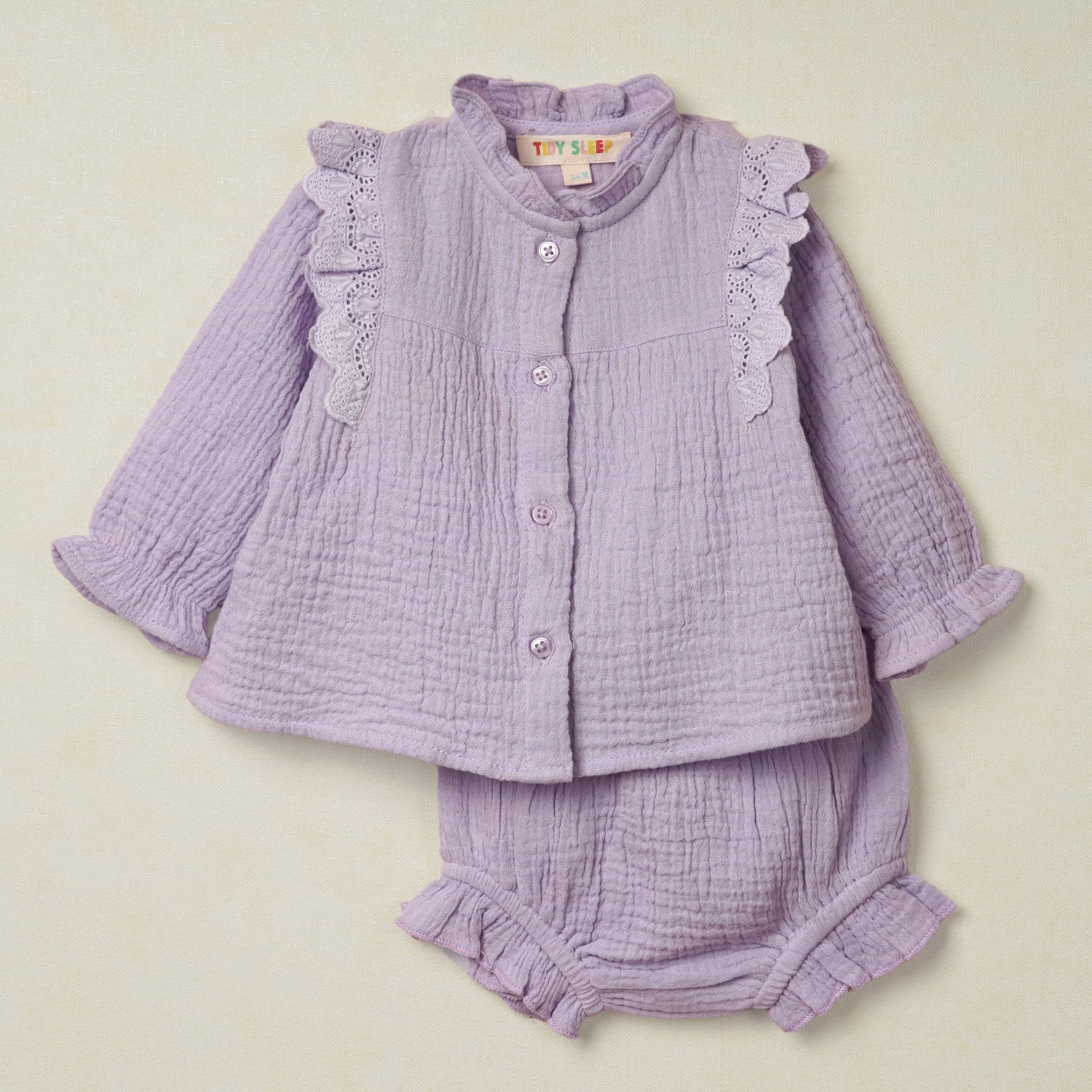 Baby outfit featuring a textured muslin top with lace ruffle details and matching bloomers in a warm peach hue in purple color.