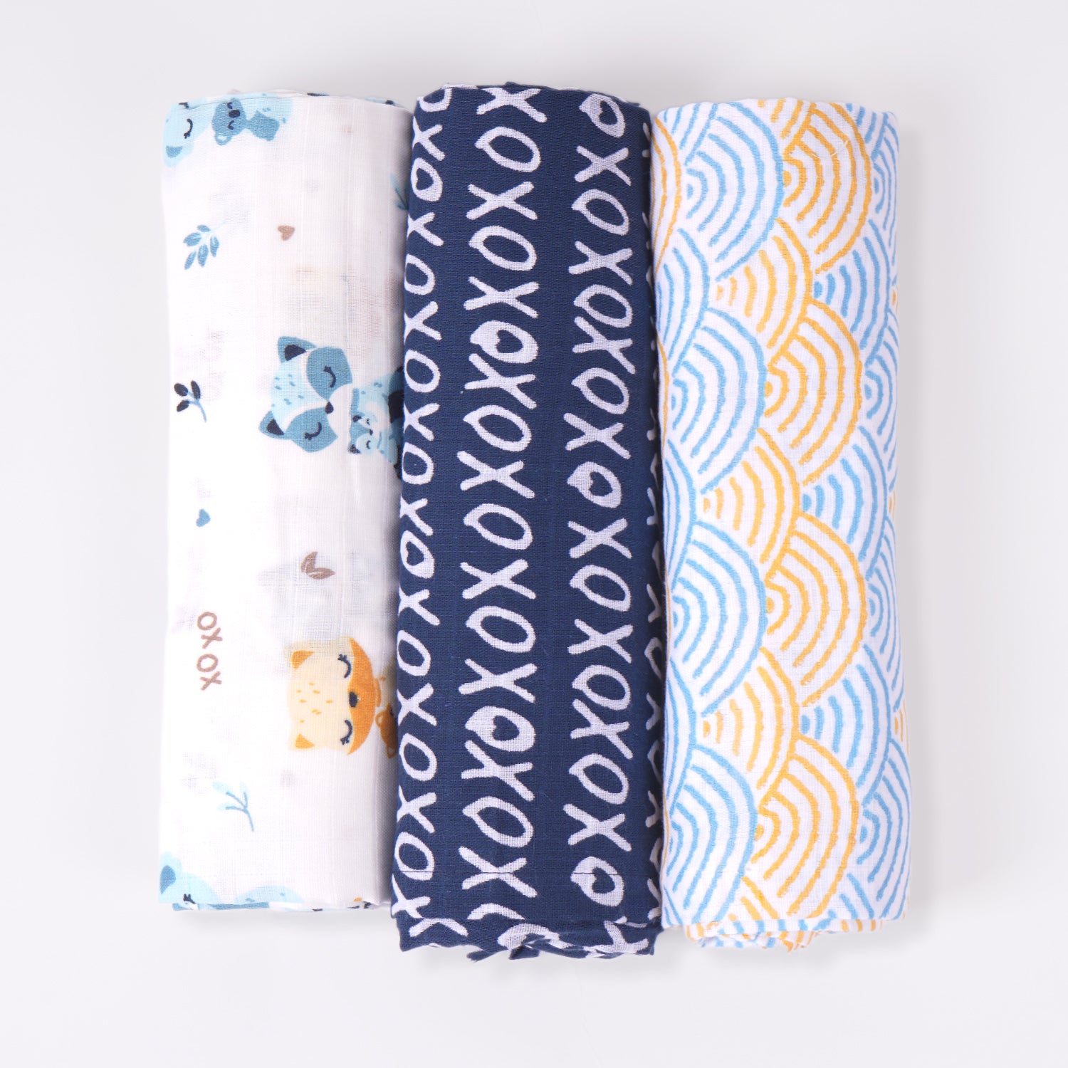 Three rolled changing mats one with a white base featuring animal prints, one navy blue with white "XOXO" patterns, and one with a blue and yellow wave-like design.