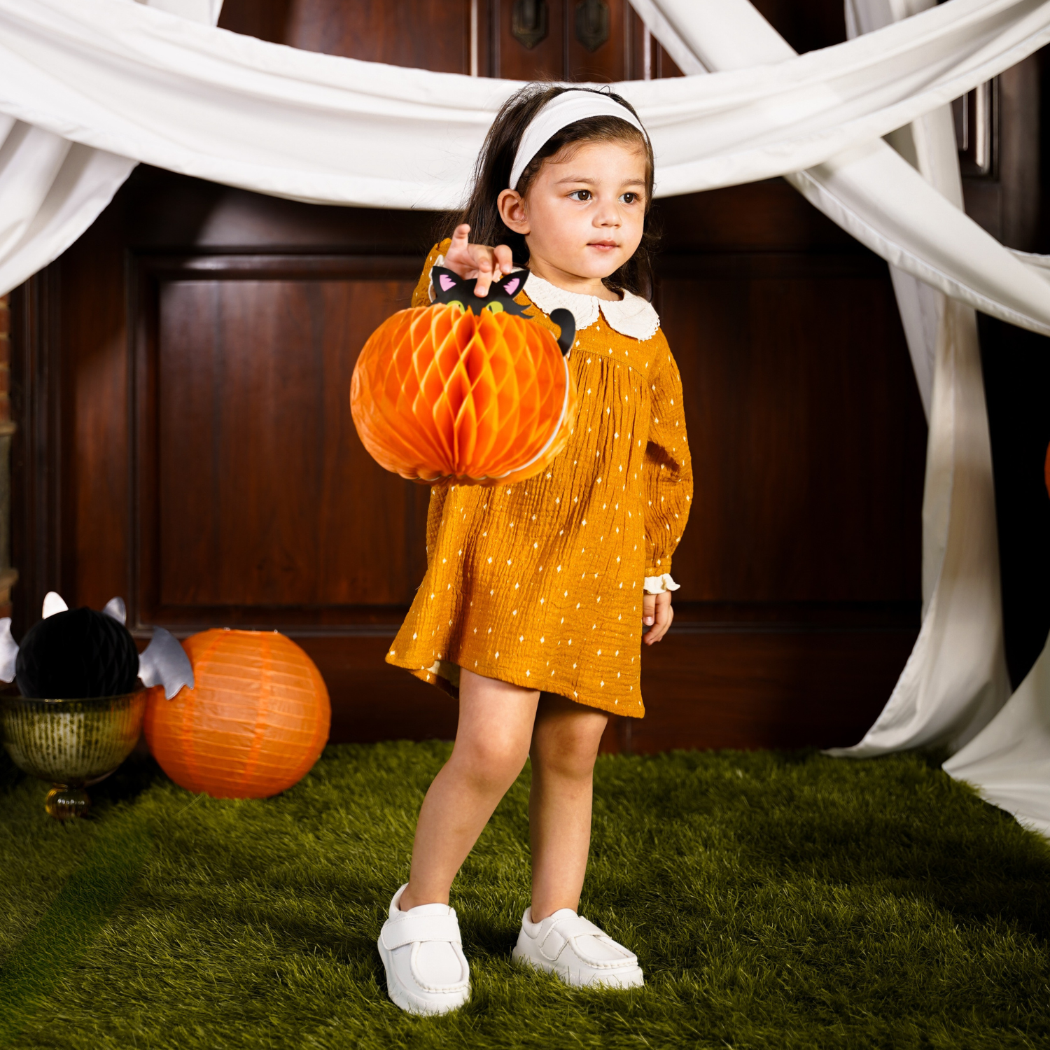 Side view of a baby girl wearing a golden-yellow frock with white polka dots, featuring a lace-collared neckline and long puffed sleeves. Perfect for a child's wardrobe.