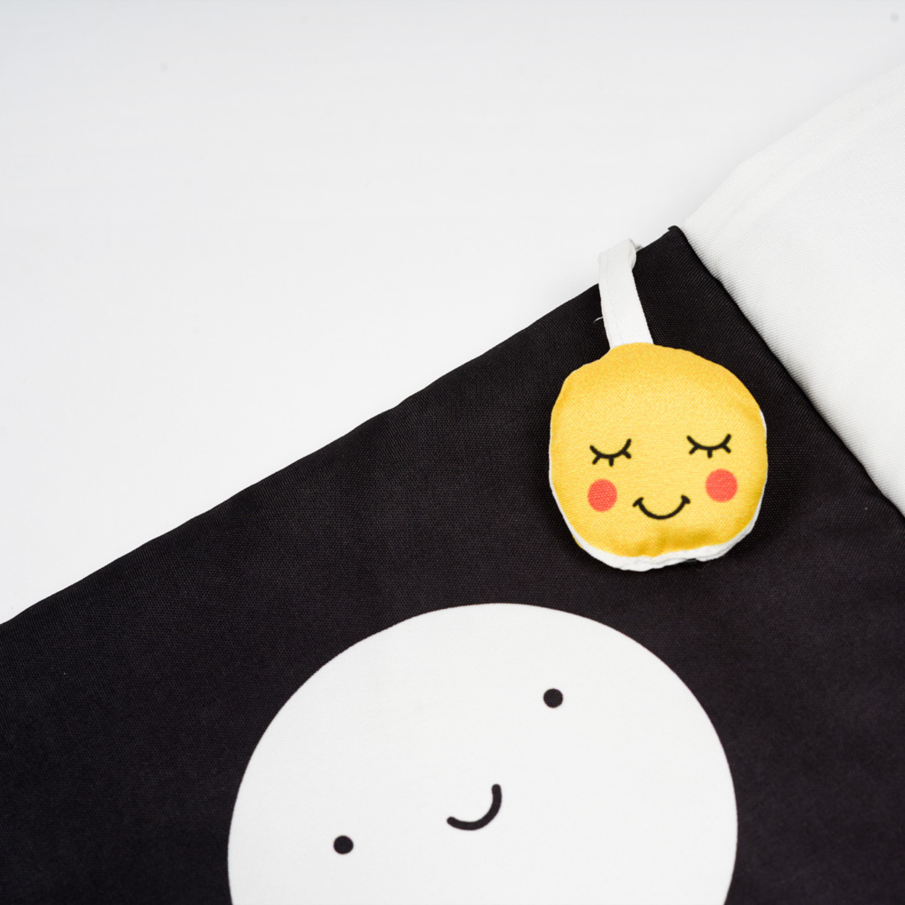 A cute, smiling moon design on a black blanket with a plush, cheerful sun tag attached at the top corner.
