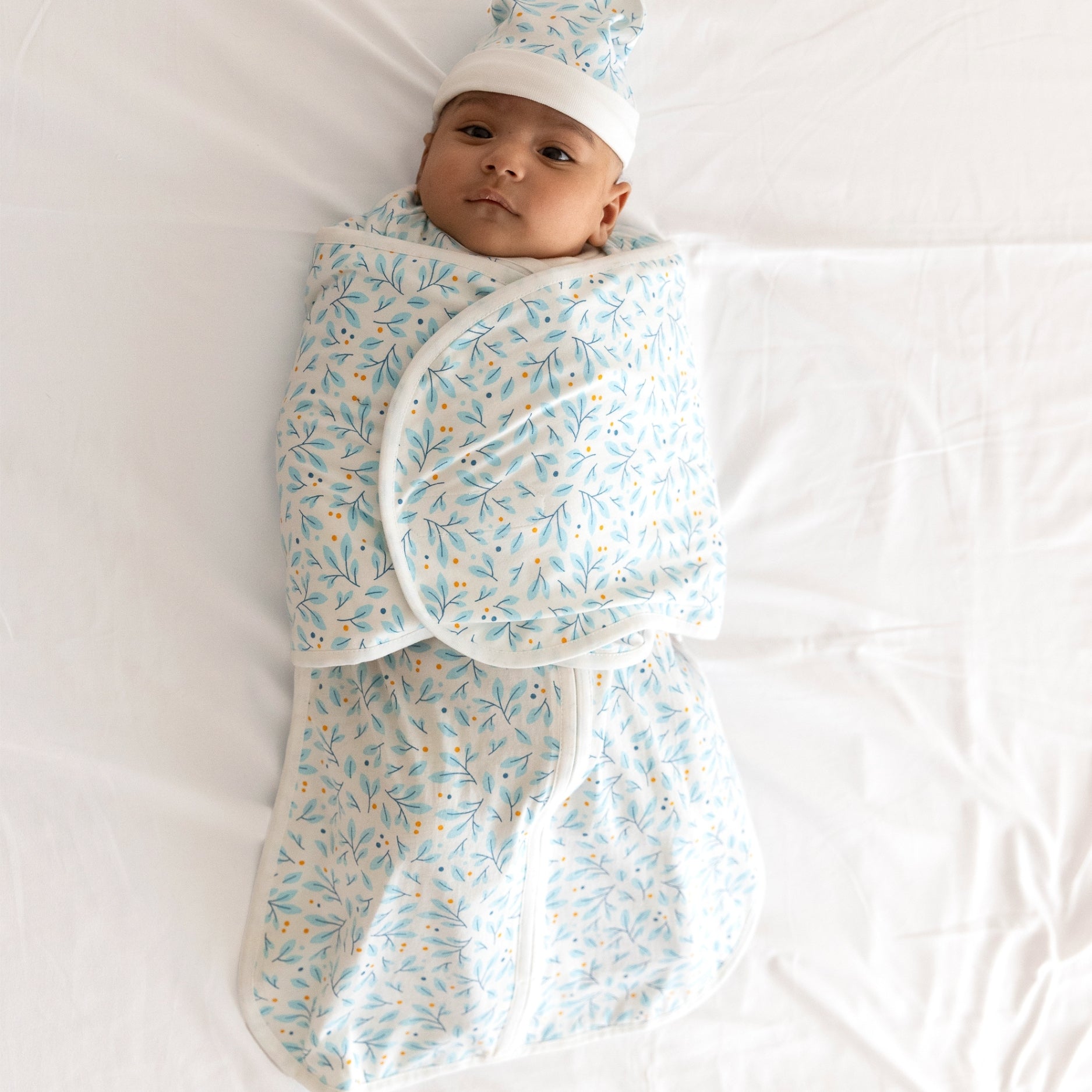 A baby swaddled in a light blue blanket with a floral pattern, resting on a white sheet.