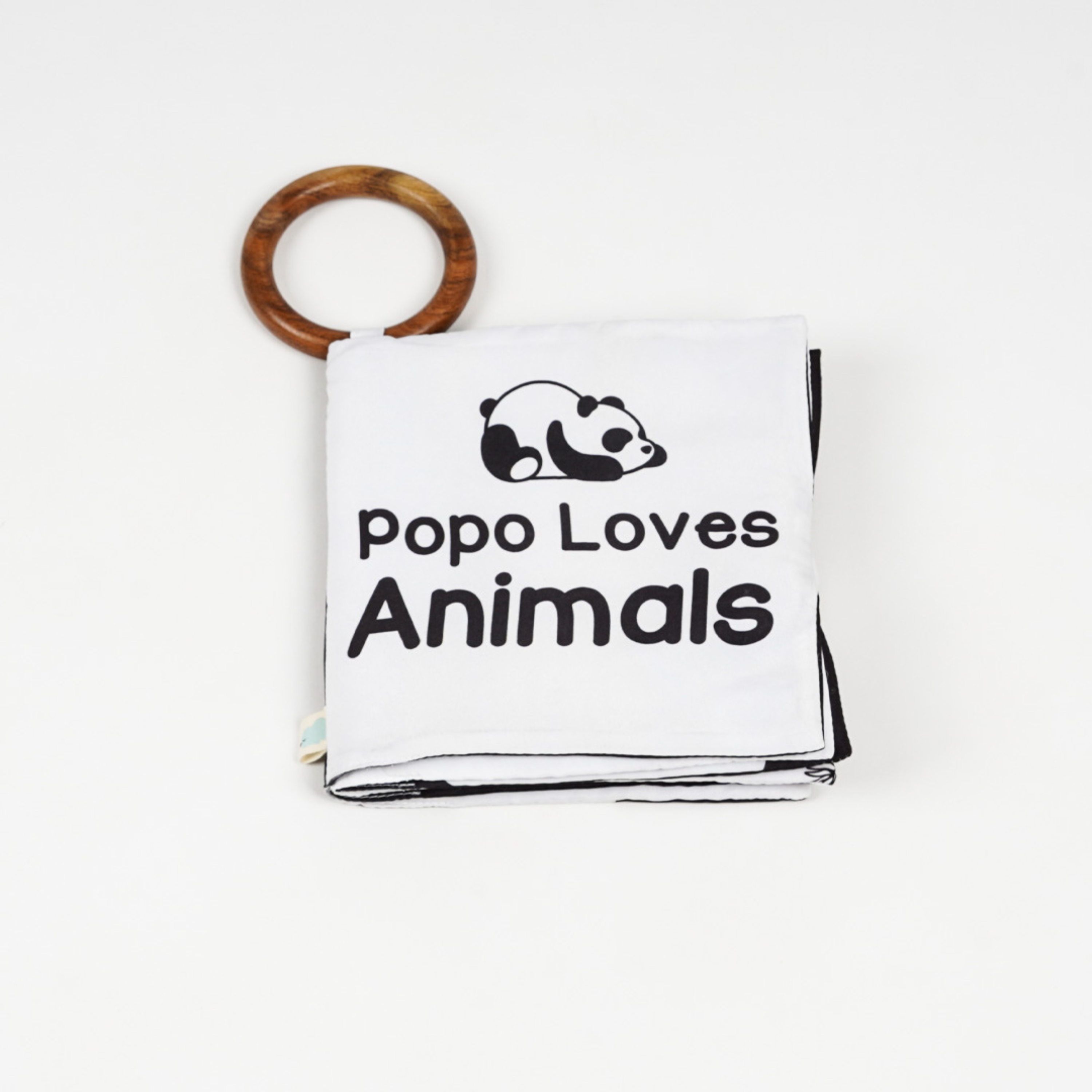 A soft cloth baby book featuring a panda graphic and the text "Popo Loves Animals," attached to a wooden teether