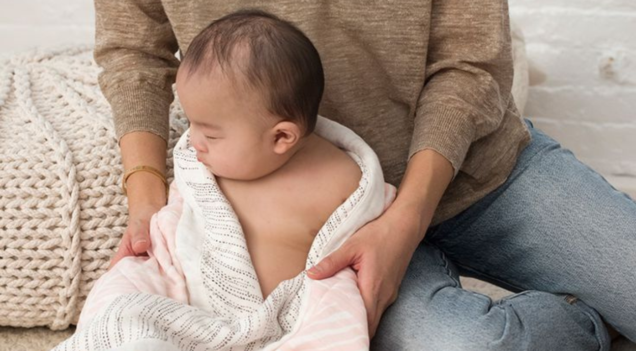 A parent gently holds a wrapped baby in a cozy setting, showcasing a soft blanket and knitted textures.