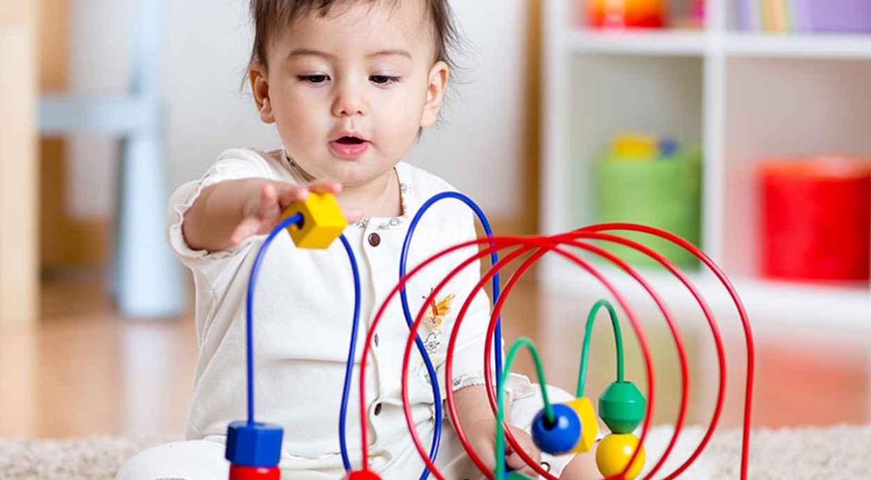 A young child reaches for a colorful wooden toy, surrounded by vibrant educational blocks in a playful indoor setting.