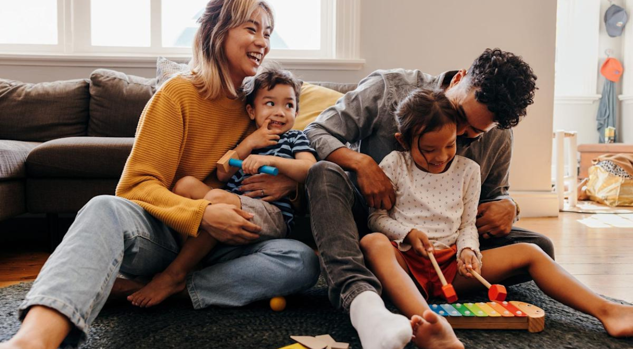 A family plays together on a living room floor, engaging with toys and a colorful xylophone, surrounded by warmth and laughter.