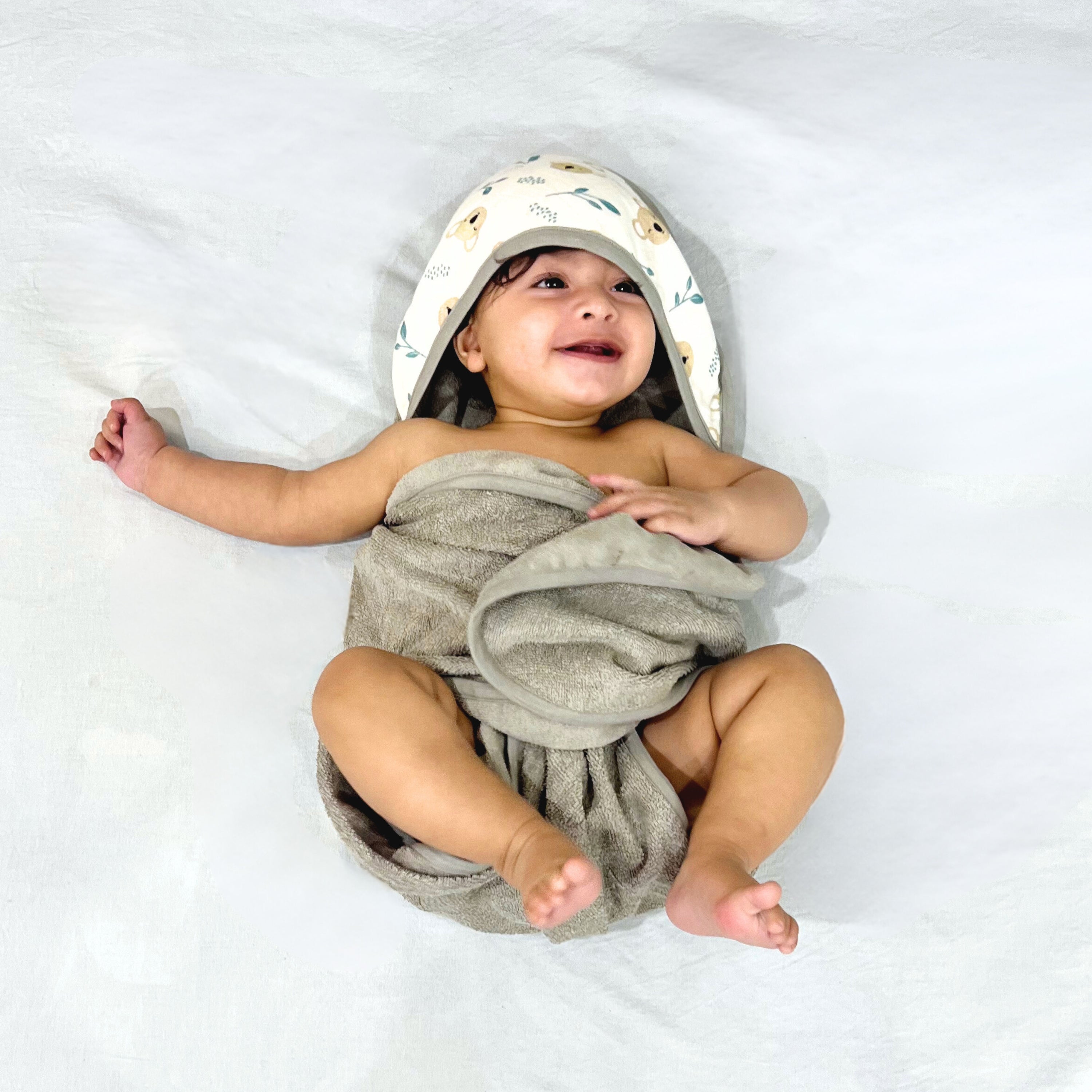 Smiling baby wrapped in a soft gray towel, lying on a white surface.
