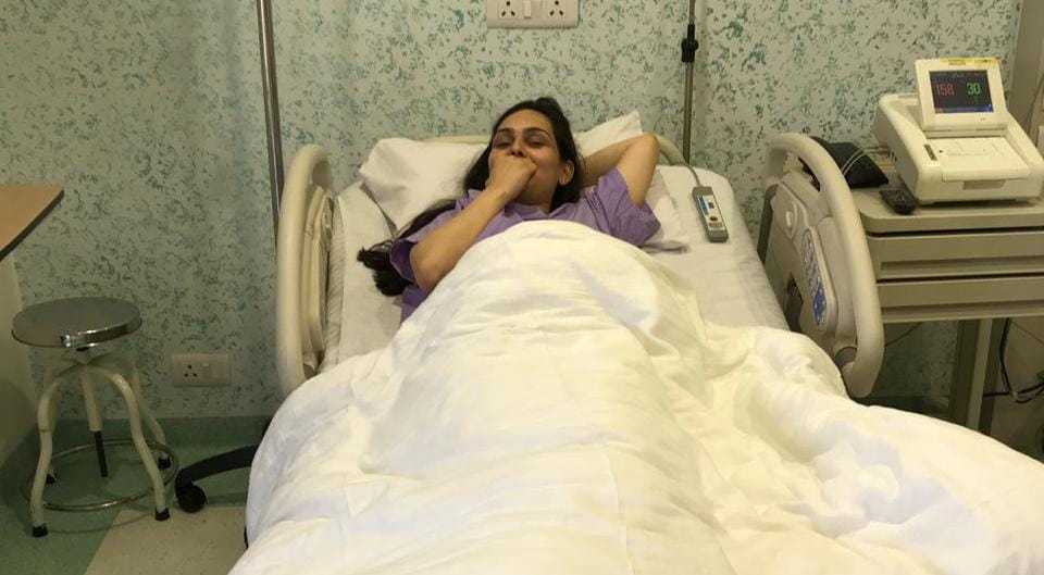 Woman resting in a hospital bed under a white blanket, with medical equipment beside her.