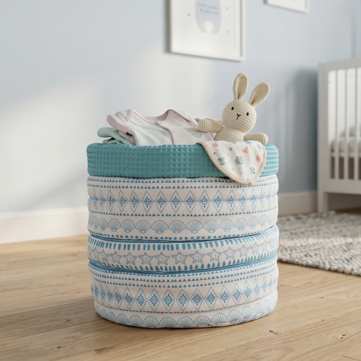 A fabric storage basket with a blue and white patterned design, filled with baby clothes and a plush bunny toy, set in a softly lit nursery.