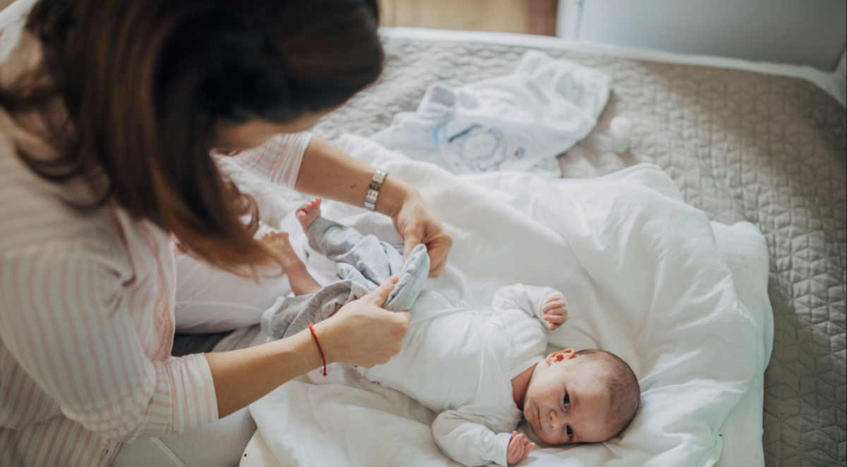 Woman dressing a baby in a white outfit on a bed